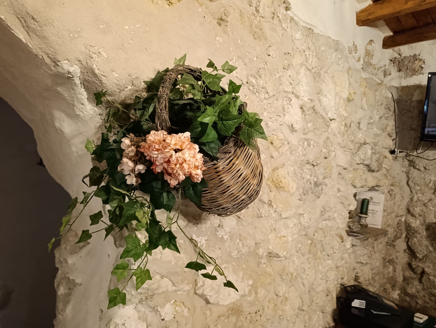 Cesto di vimini con edera e fiori appeso a una parete in pietra della trattoria