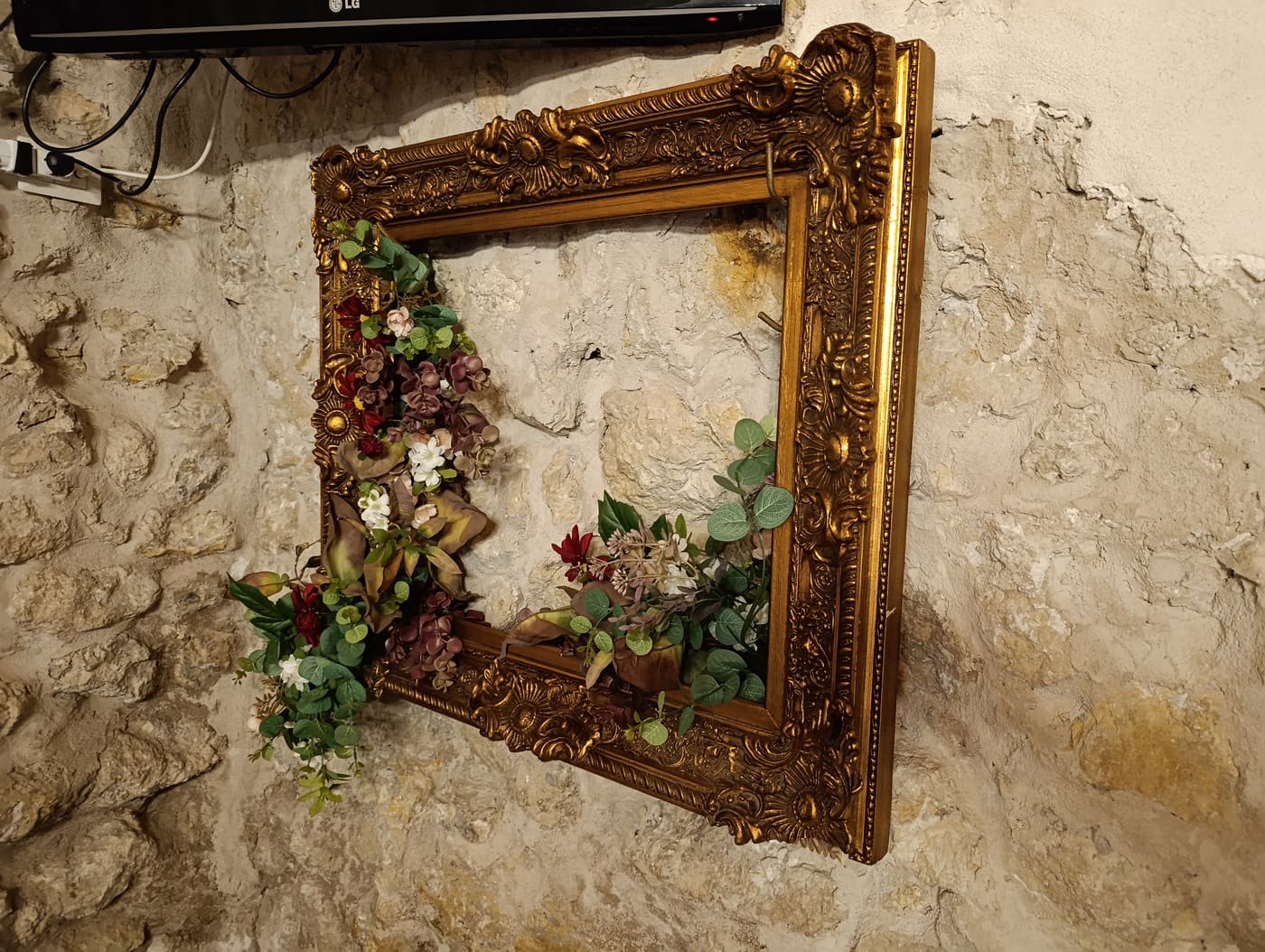Cornice barocca dorata vuota con una composizione di fiori secchi ed eucalipto, appesa al muro in pietra