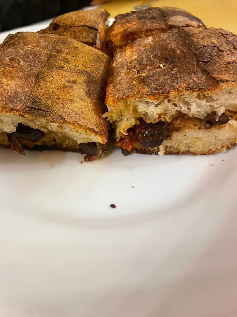 Focaccia siciliana ripiena cotta al forno, tagliata a metà: dentro olive nere e pomodori secchi