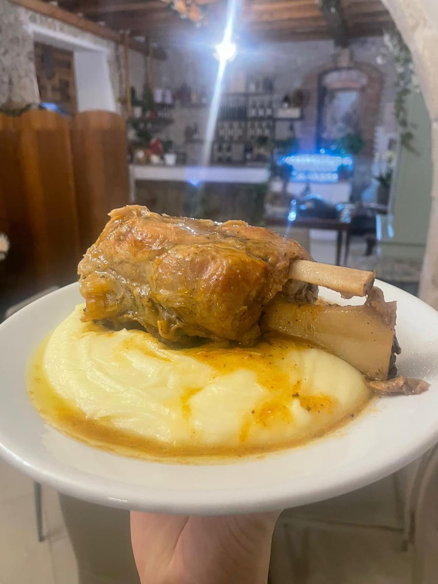 Stinco di maiale al forno con il suo fondo di cottura, servito su un letto di purè di patate