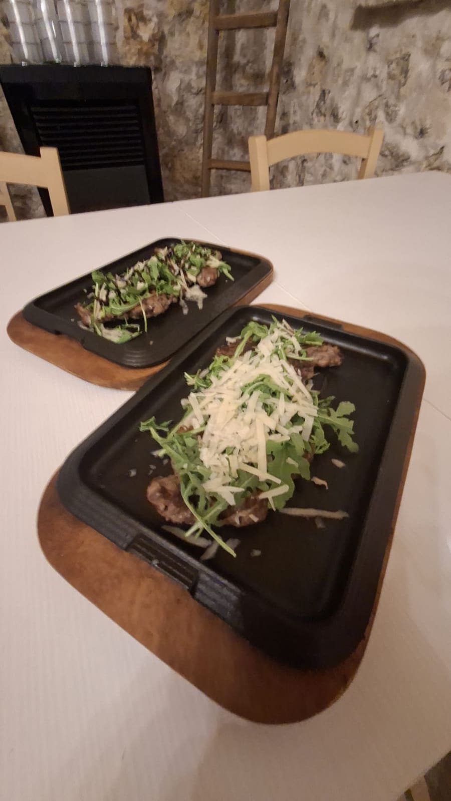 Tagliata di vitello su piastra in ghisa, coperta di rucola e scaglie di formaggio