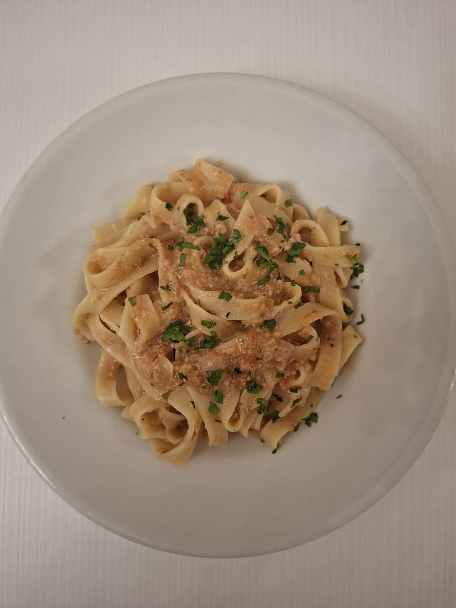 Tagliatelle Sicilia in Bocca con prosciutto cotto e pomodori secchi, spolverate di prezzemolo, in un piatto bianco