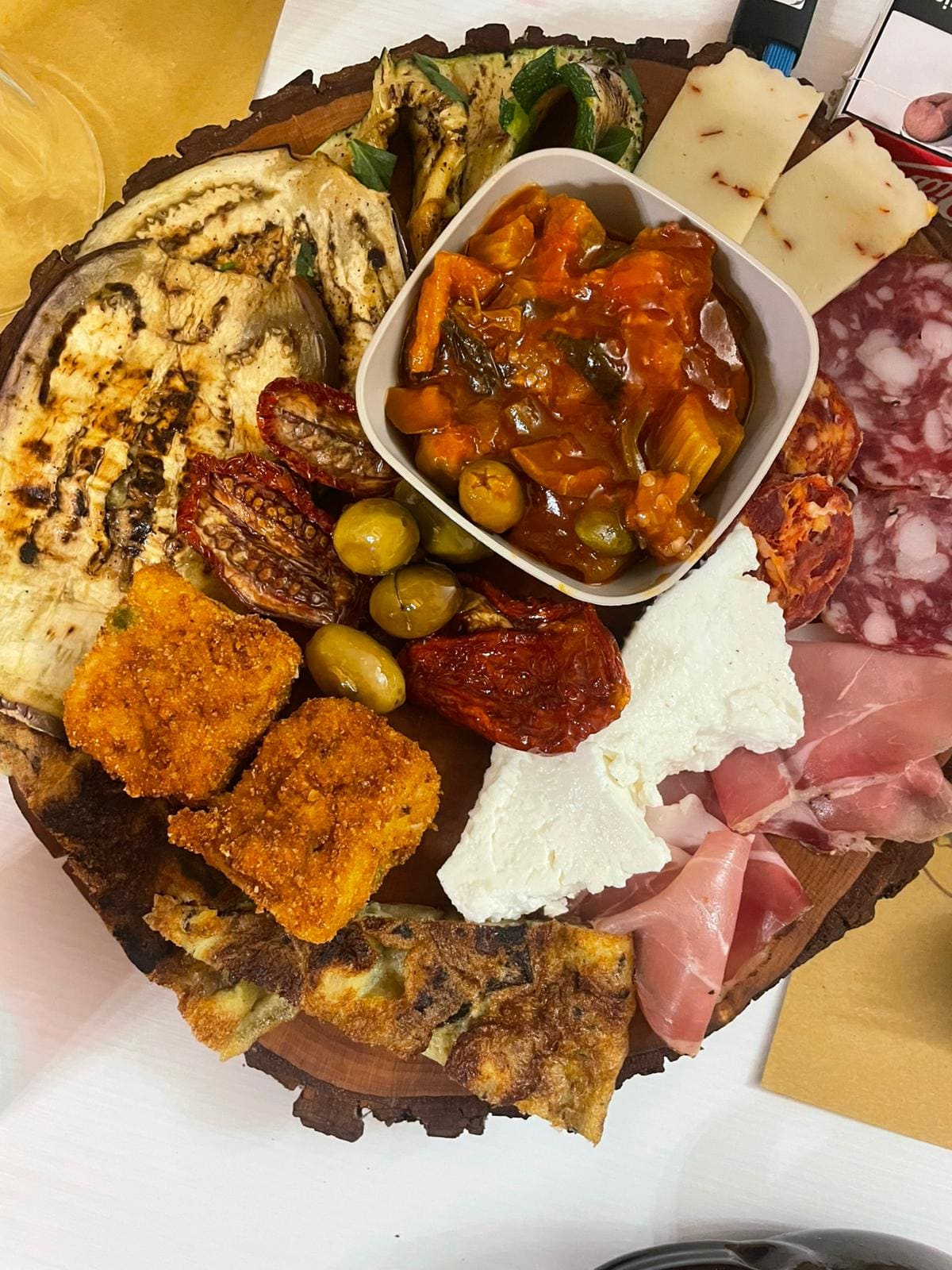 Il tagliere dell'antipasto Sicilia in Bocca su un tronco di legno: melanzane e zucchine grigliate, caponata, pomodori secchi, olive, formaggio al peperoncino, ricotta, salame, prosciutto crudo, frittata e sfizi fritti