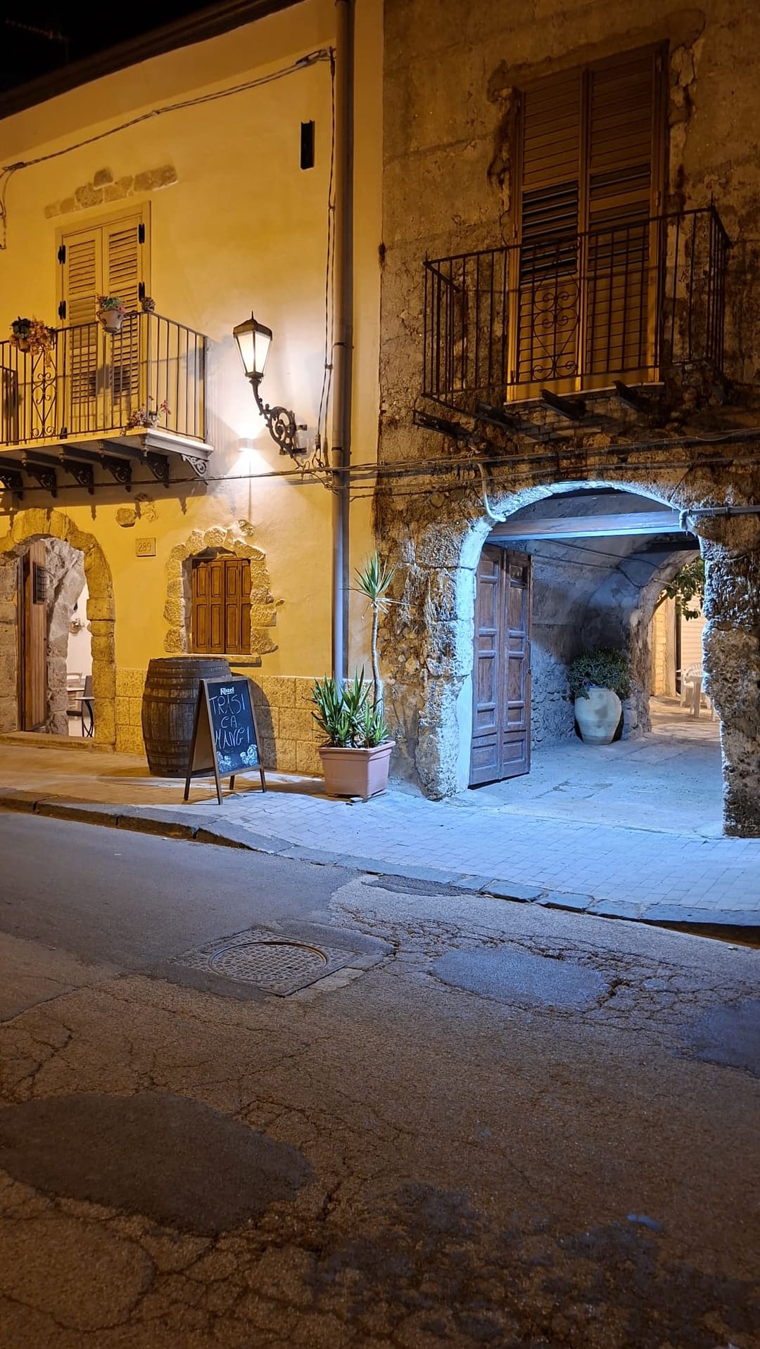 Di sera, la lavagna «Trasi ca mangi» accanto a una botte di legno e il grande portone ad arco in pietra che porta al cortile