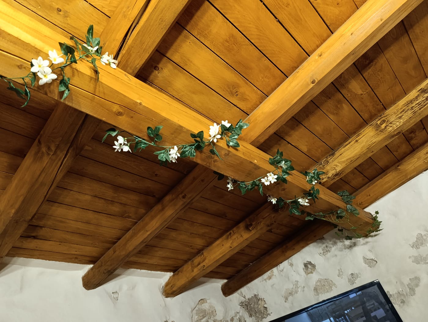 Soffitto della sala con travi di legno a vista, decorato con tralci di fiori bianchi