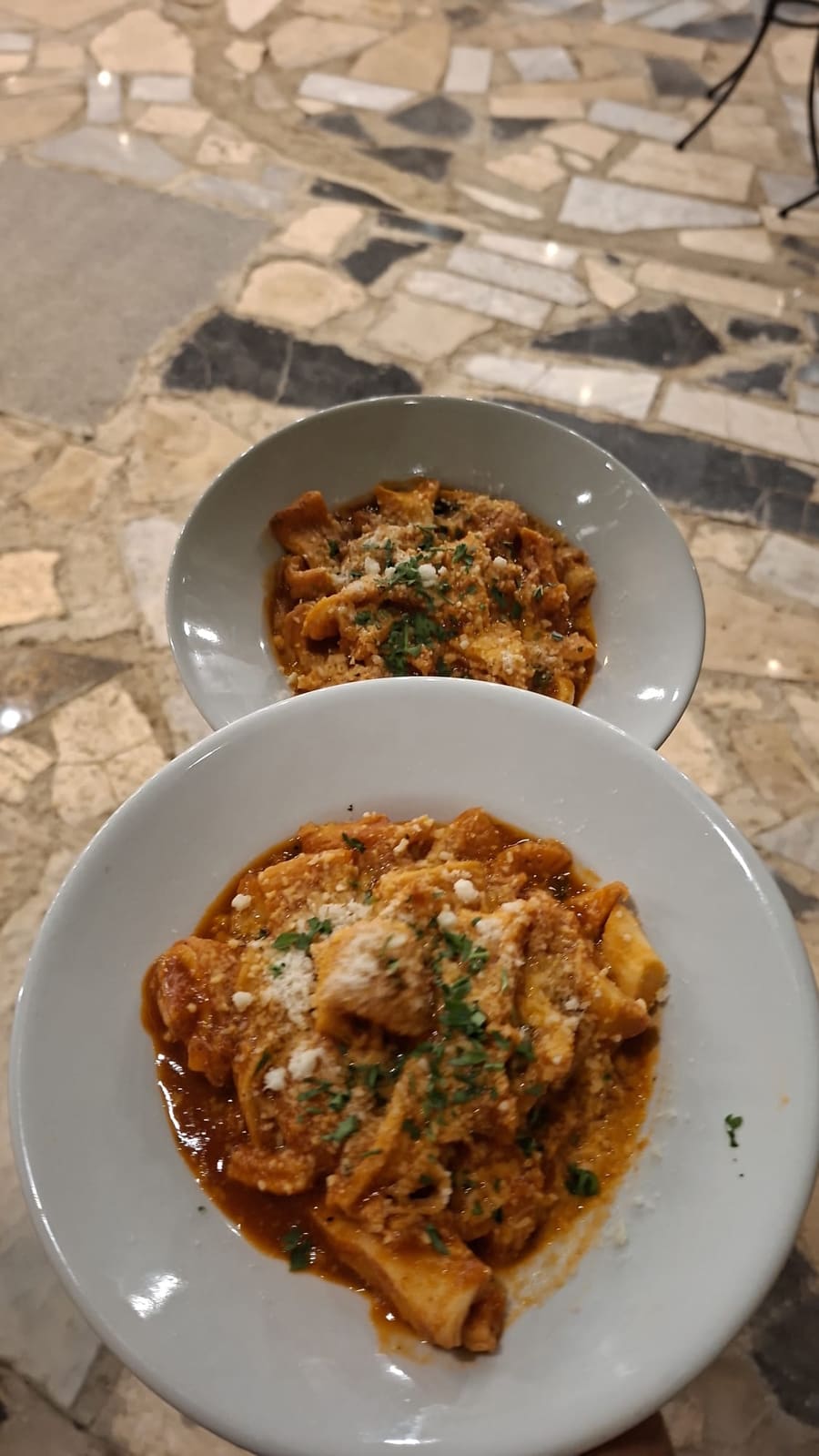 Due piatti di trippa al sugo di pomodoro con formaggio grattugiato e prezzemolo, su un pavimento in marmo a mosaico